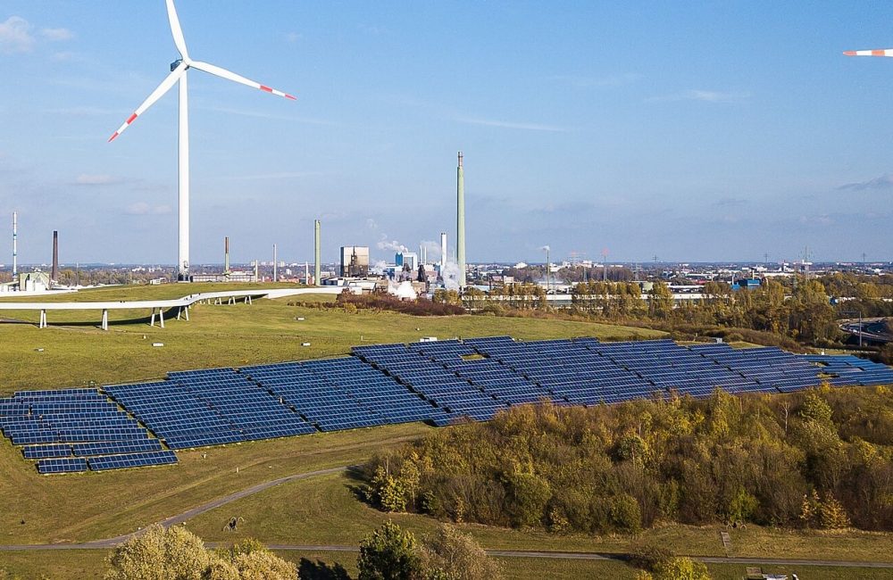 Foto von PV Freiflächenanlage auf dem Energieberg Georgswerder aus der Luft. Im Hintergrund Windräder und Skyline mit Industrie.