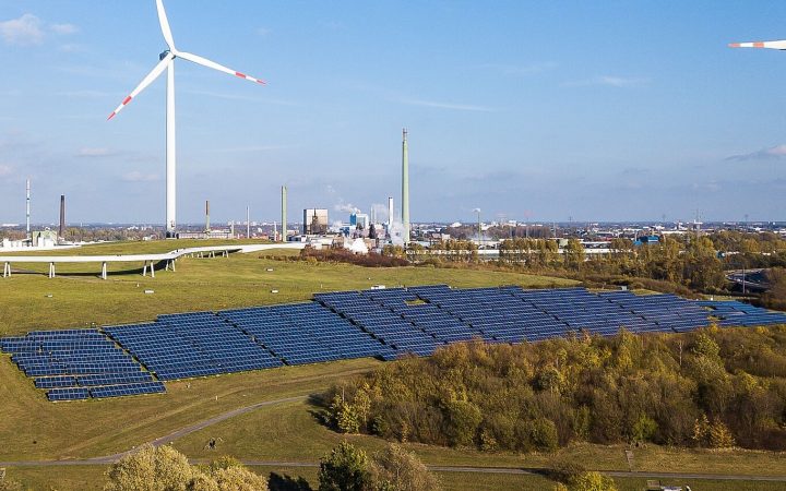 Foto der PV Freiflächenanlage auf dem Energieberg Georgswerder aus der Luft. Im Hintergrund Windräder und Skyline mit Industrie.